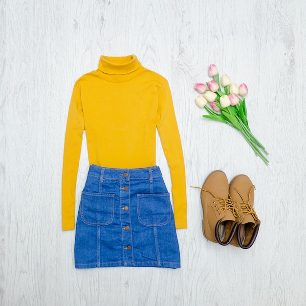 Mode concept. gele coltrui, blauwe rok, laarzen en roze tulpen. hout achtergrond