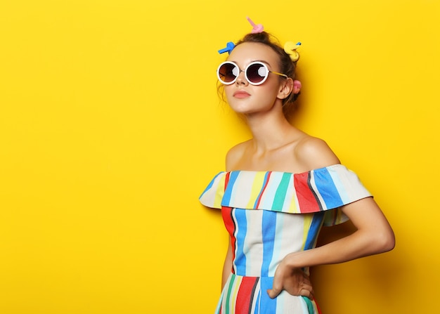 Mode coole vrouw poseren in zonnebril op geel. Jonge hipster vrouw met krulspelden in haar haar