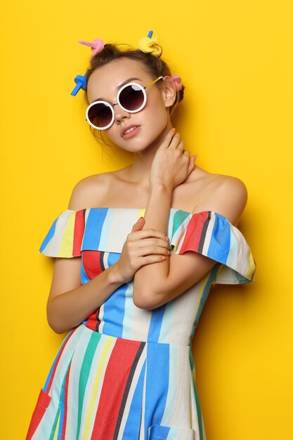 Mode coole vrouw poseren in zonnebril op geel. Jonge hipster vrouw met krulspelden in haar haar