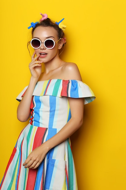 Mode coole vrouw poseren in zonnebril op geel. Jonge hipster vrouw met krulspelden in haar haar