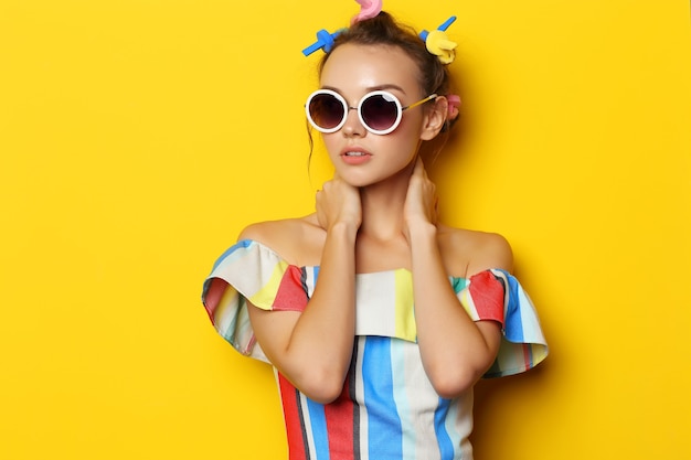 Mode coole vrouw poseren in zonnebril op geel. Jonge hipster vrouw met krulspelden in haar haar