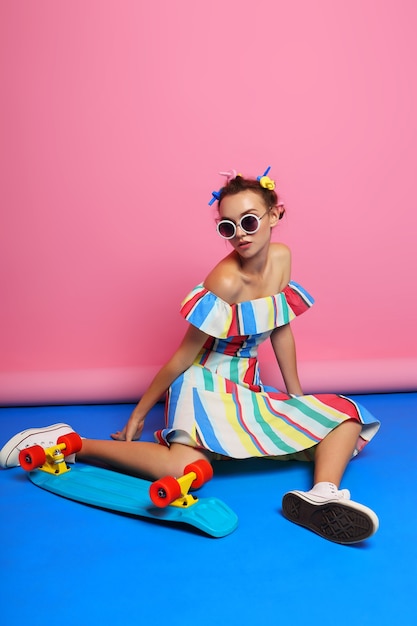 Mode coole vrouw poseren met skateboard. Jonge hipster vrouw met krulspelden in haar haar, zonnebril, witte sneakers. studio opname