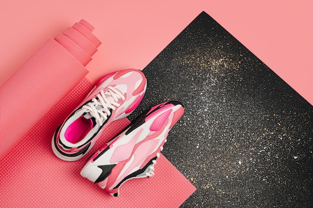 Mode dames sneakers met een roze yoga mat op zwarte achtergrond. Gezond levensstijlconcept. Platliggend bovenaanzicht kopiëren