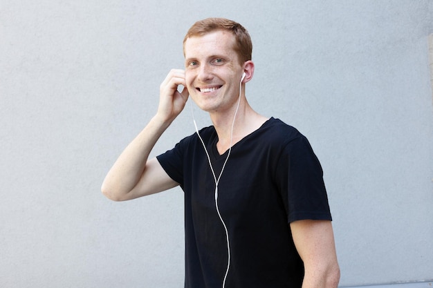 Mode emoties en mensen concept close-up portret van een roodharige mooie mannelijke jongen sproetenliedjes op slimme telefoon met koptelefoon dansen gebaren gelukkig geïnspireerd door favoriete muziek