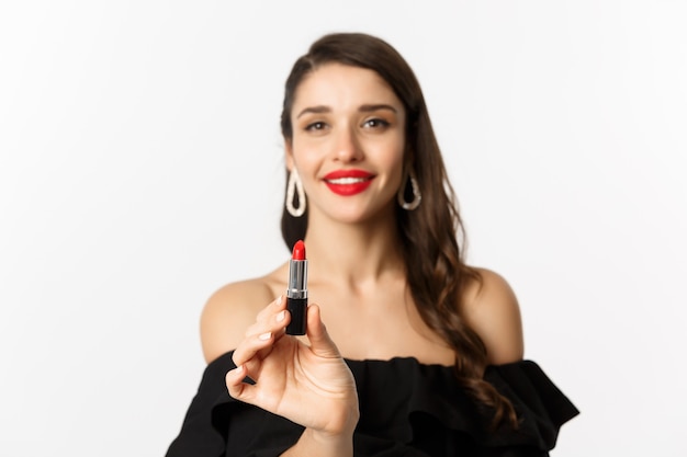 Mode en beauty concept. Mooie vrouw in zwarte jurk met rode lippenstift en glimlachen, staande op een witte achtergrond