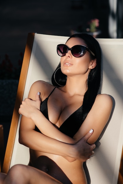 Mode foto van mooie gebruinde vrouw met zonnebril in elegante zwarte bikini