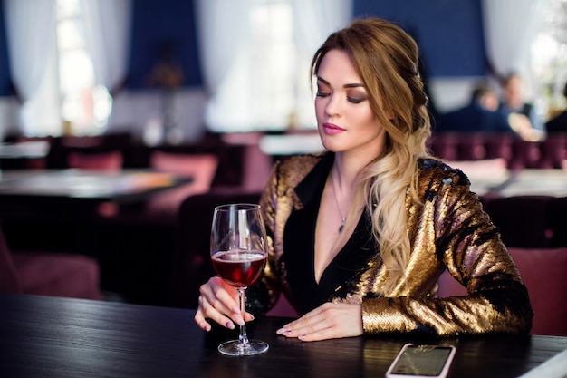 mode foto van mooie sensuele vrouw met krullend haar in elegante kleding in café, wijnstok drinken