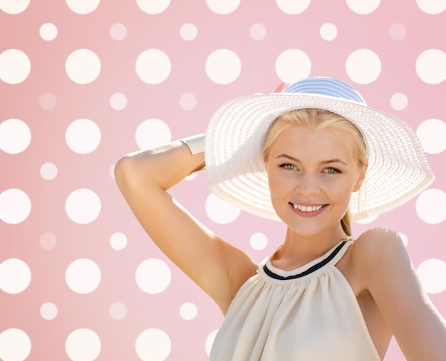 mode, geluk en mensenconcept - mooie glimlachende vrouw in witte zomerhoed over roze en witte stippenpatroonachtergrond