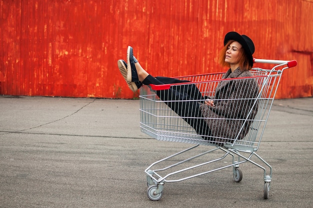 Foto mode hipster cool meisje in winkelwagen met plezier tegen de kleurrijke oranje muur.