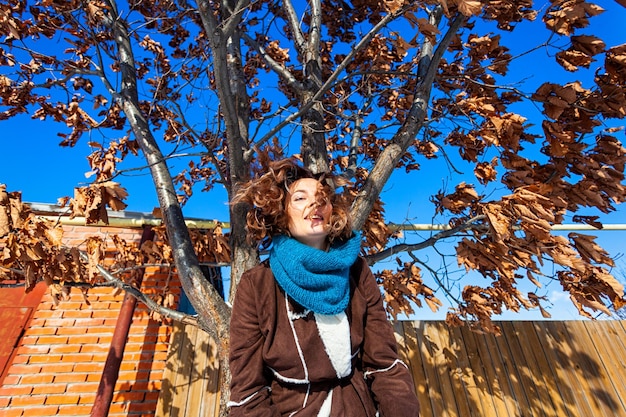 Mode levensstijl portret van jonge trendy vrouw gekleed in warme stijlvolle kleding poseren en glimlachen op een achtergrond van eik met vergeelde bladeren portret van vrolijke vrouw