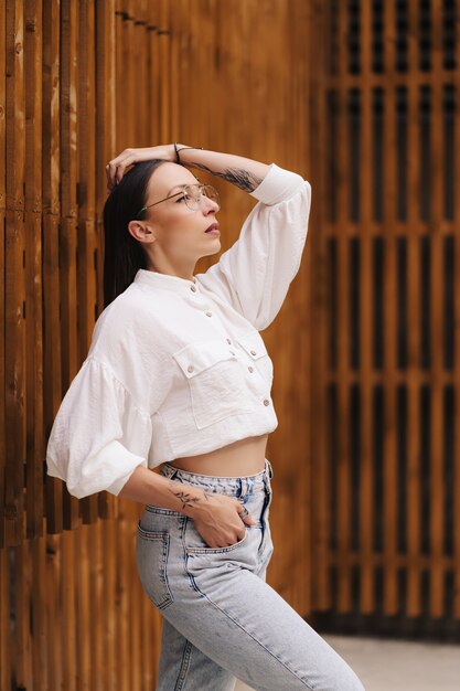 Mode portret van een aantrekkelijke brunette met steil haar. vrouw gekleed in een witte blouse en een bril poseren