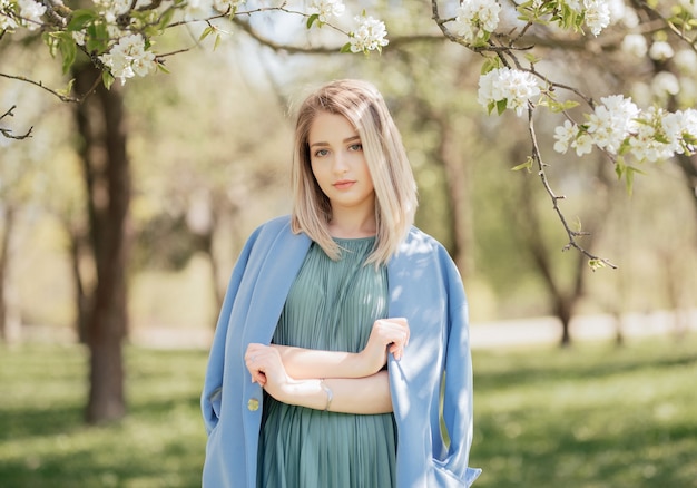 Mode portret van een blonde vrouw in groene jurk en blauwe jas in lente park