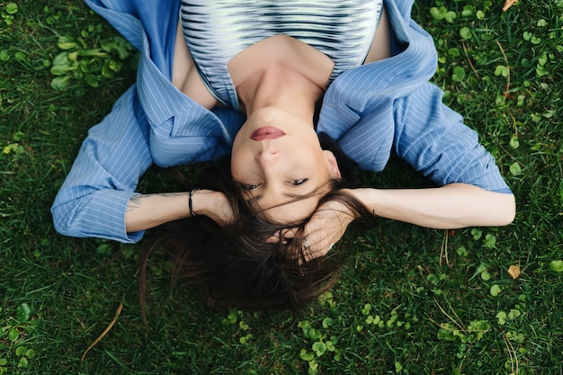 Mode portret van een jonge vrouw gekleed in een blauw gestreept jasje. vrouw ligt op een groen gazon in een park in de stad