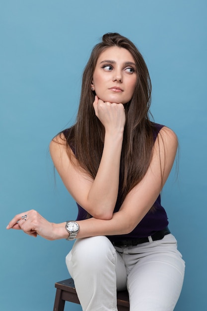 Mode portret van een jonge vrouw in een mouwloos onderhemd en lichte broek op een blauwe muur