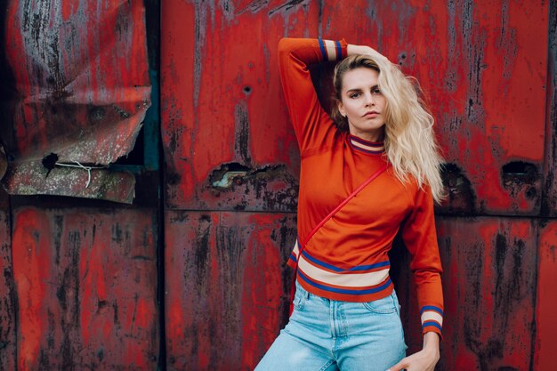 mode portret van jonge mooie schattige vrouw model. Vreemde bizarre vreemde ongewone schattige ondeugende blonde babe die zich voordeed op oude roestige metalen poort. Mooi ogende vrouw in trendy kleding.