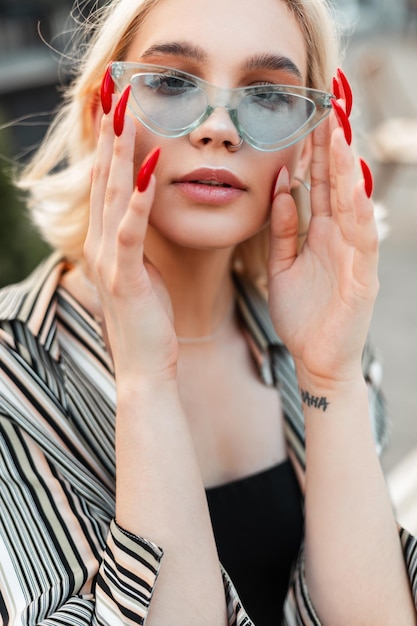 Mode portret van jonge tondel blonde vrouw zet stijlvolle blauwe zonnebril op in de stad