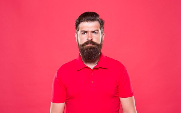 Mode portret van man mannelijke schoonheid en mode baan van kassier trendy en brute gezichts baard zorg bebaarde man casual stijl professionele kapper rode achtergrond volwassen hipster serieuze blik