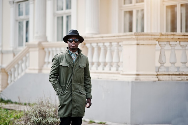 Mode portret van zwarte Afro-Amerikaanse man op groene jas mantel en zwarte hoed achtergrond geel herenhuis