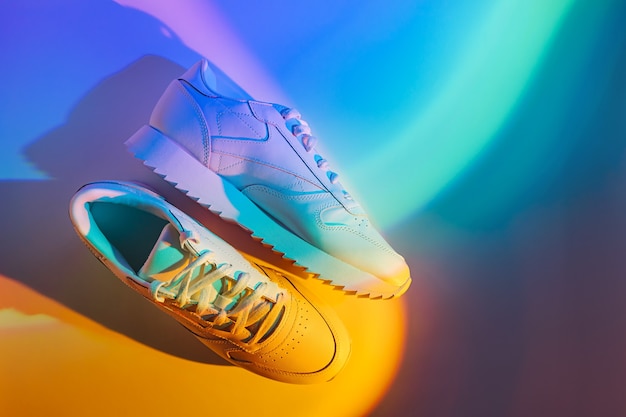 Mode sneakers op levendige abstracte achtergrond. Sportschoenen in neonlicht. Blauw en oranje verloop.