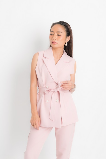 Mode-stijl catalogus kleding voor zakenvrouw zwart lang haar natuurlijke make-up slijtage roze pak kostuum perfecte lichaamsvorm pak bij studio shoot op witte achtergrond en schaduw.