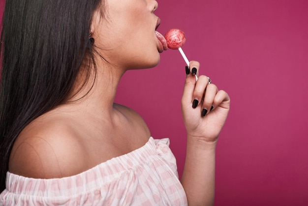 Mode swag portret van mooie elegante aziatische vrouw in roze jurk met lolipop op lichte achtergrond