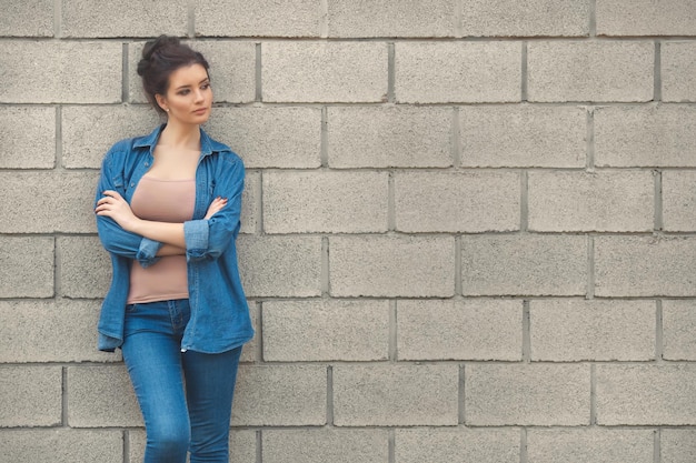 Mode vrouw in totale denim kleding staande in de buurt van lege bakstenen muur mockup kopie ruimte