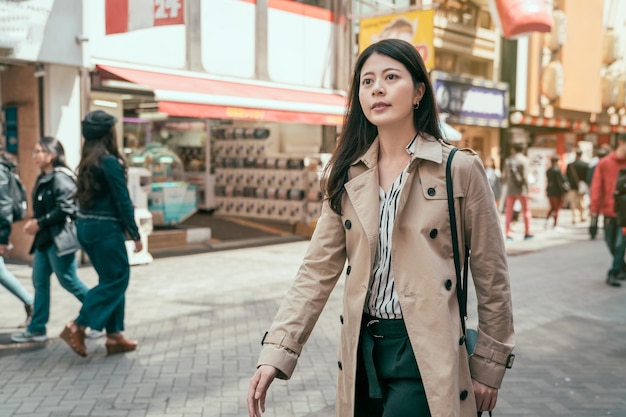 Mode vrouw portret van vrij trendy meisje wandelen in de stad osaka in japan. lentestraat in dotonbori. lachende vrouw ontspannen op de weg met Japanse capsule speelgoed machine winkel op de achtergrond