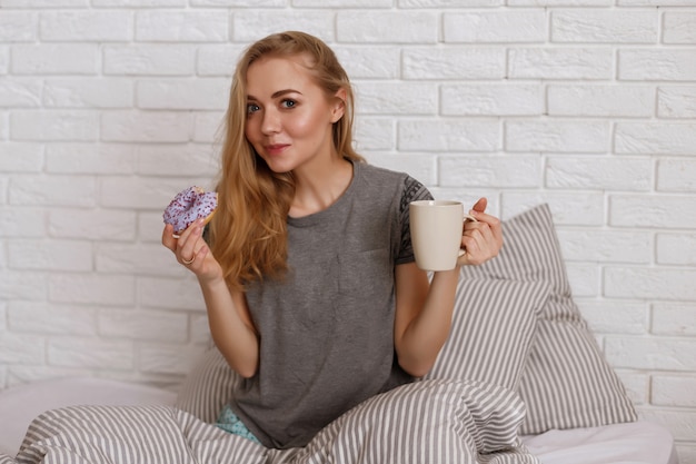 model in bed in the morning eats a donut and drinks coffee