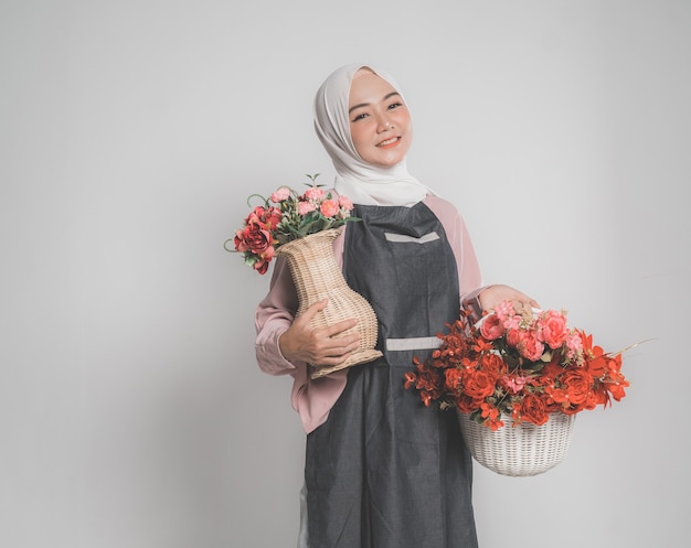 Model draagt hijab, met een bloem op een beige geïsoleerde achtergrond. Stijlvolle moslimvrouw met een emmer met bloem