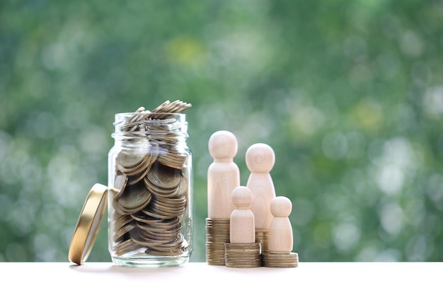 Model family and stack of coins money in the glass bottle on natural green backgroundSave money for prepare in future and family finance concept