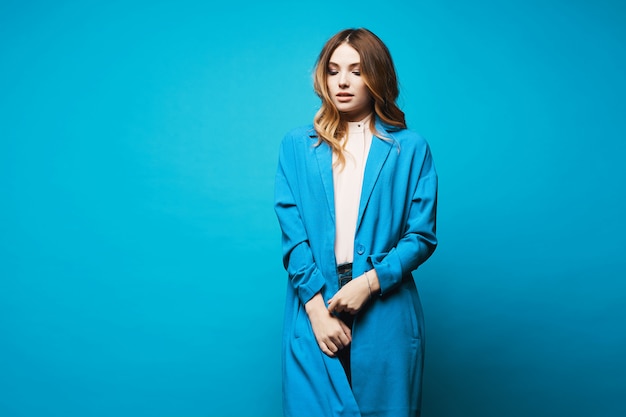 Model girl in blue coat and blouse isolated at blue background with copy space. Female fashion. Beauty concept. European hipster girl.