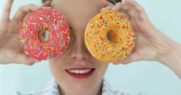 Model girl holding colorful pink donuts against her eyes. 