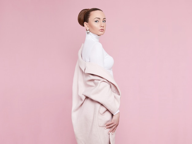 A model girl in a pink coat looks at the camera and poses