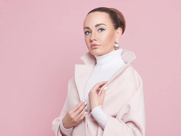 A model girl in a pink coat looks at the camera and poses