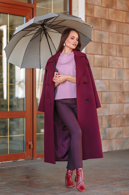 Photo a model girl showing fashionable outerwear with an umbrella in her hand on the street on the veranda of a summer cafe clothes for the showroom