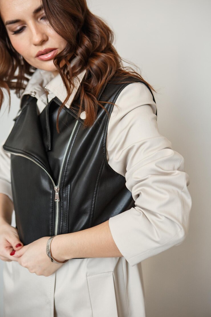 モデルの女の子は、服を宣伝するスタジオの背景に立っていますベージュのスーツと革のジャケットの女の子