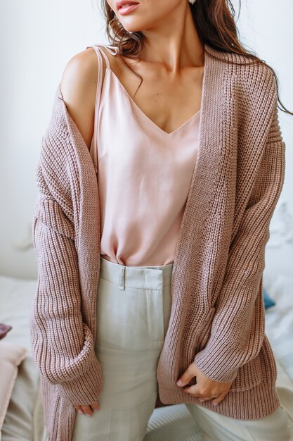 Model girl in a stretched knitted jacket on the bed. 