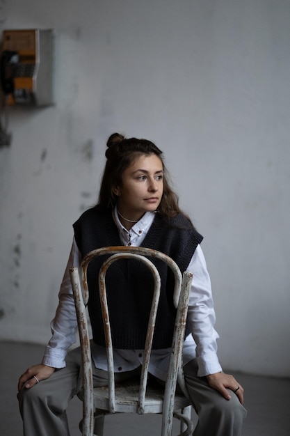 A model girl with long dark wavy hair poses in a white shirt and a gray knitted sweater vest