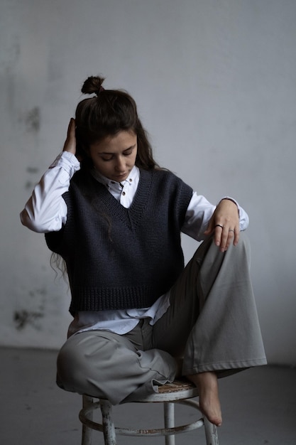 Una ragazza modello con lunghi capelli ondulati scuri posa con una camicia bianca e un gilet grigio lavorato a maglia
