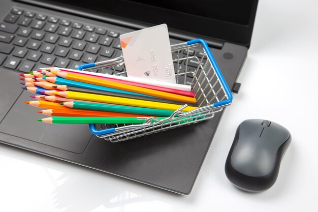 Model of a grocery cart with colored pencils on the background of a laptop Product search online shopping websites