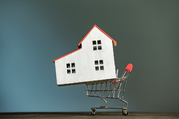 Model home on the shopping cart. Buy house concept. Dark background, front view.