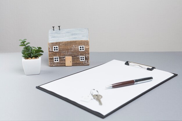 Model house and keys with clipboard on grey surface