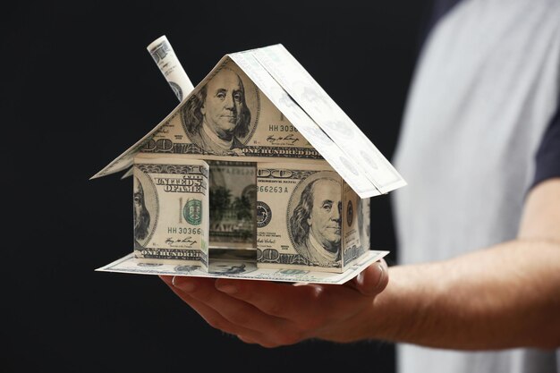 Model of house made of money in male hands on dark background