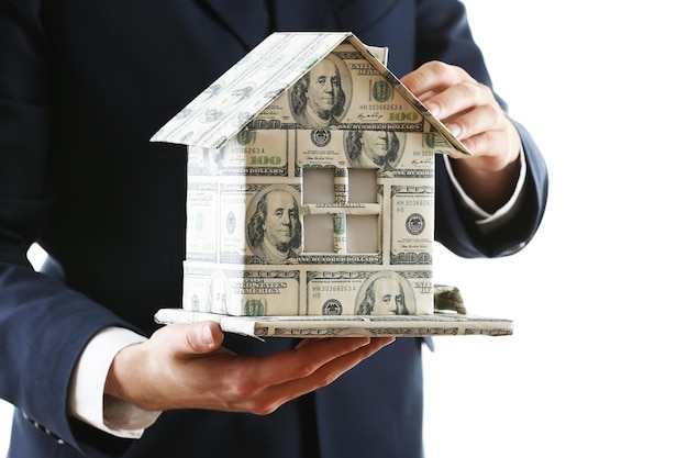 Model of house made of money in male hands isolated on white background