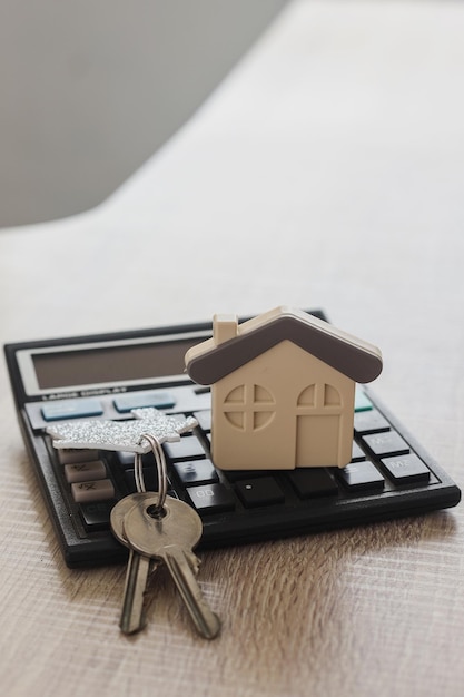 Model of house with calculator and key on wooden table. Real estate concept.