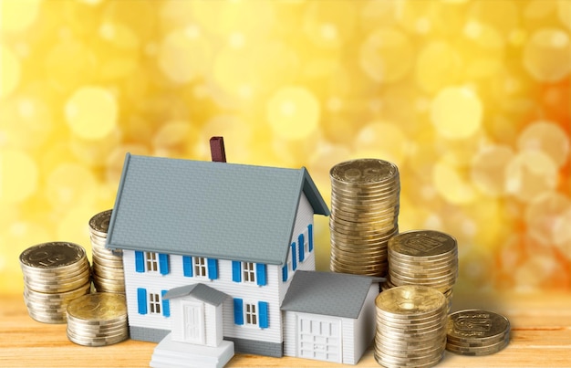 Model of house with coins on wooden background