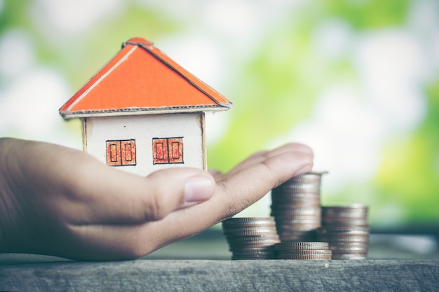 Model of house with coins on wooden table on blurred background