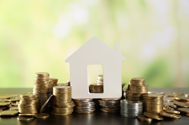 Model of house with coins on wooden table on blurred background