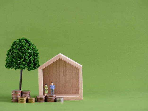 Model house with miniature people and coins on green background. Space for text