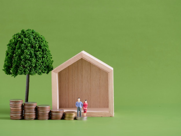 Model house with miniature people and coins on green background. Space for text